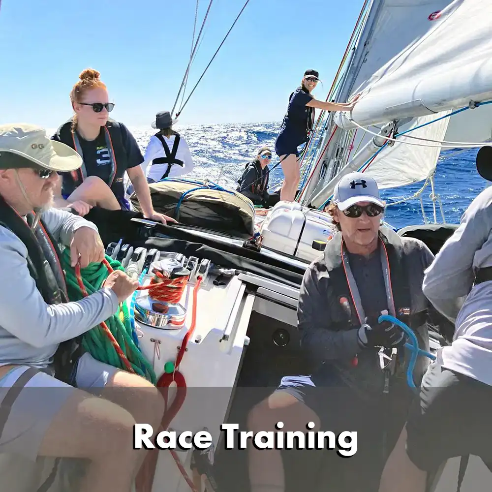 Équipage effectuant un exercice d'entraînement à l'homme à la mer sur un voilier. Une personne portant un casque et un gilet de sauvetage est hissée à bord à l'aide d'un harnais de levage et d'une ligne de sauvetage. Le voilier est en mer avec une côte montagneuse visible à l'arrière-plan.  