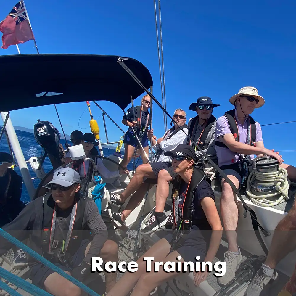 Membres de l'équipage d'un voilier en train de s'entraîner à la course, portant des gilets de sauvetage et des harnais. Certains manipulent activement les lignes et les treuils, tandis que d'autres observent et préparent les manœuvres. Le voilier navigue dans des eaux d'un bleu profond, avec un ciel clair au-dessus de la tête et un drapeau rouge flottant à l'arrière.  